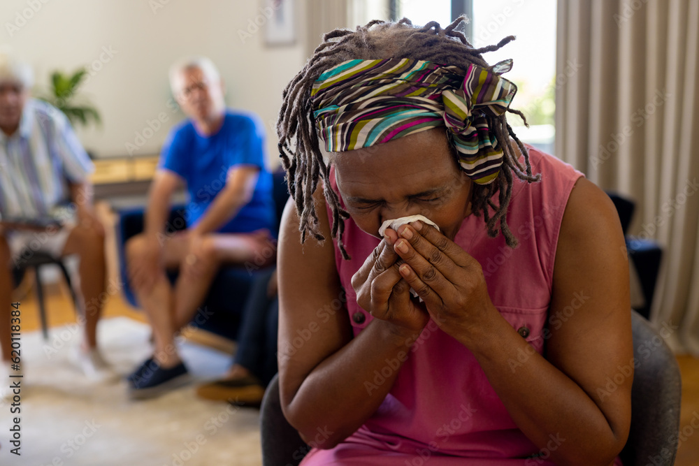 Distressed senior biracial woman holding tissue and crying in group therapy session