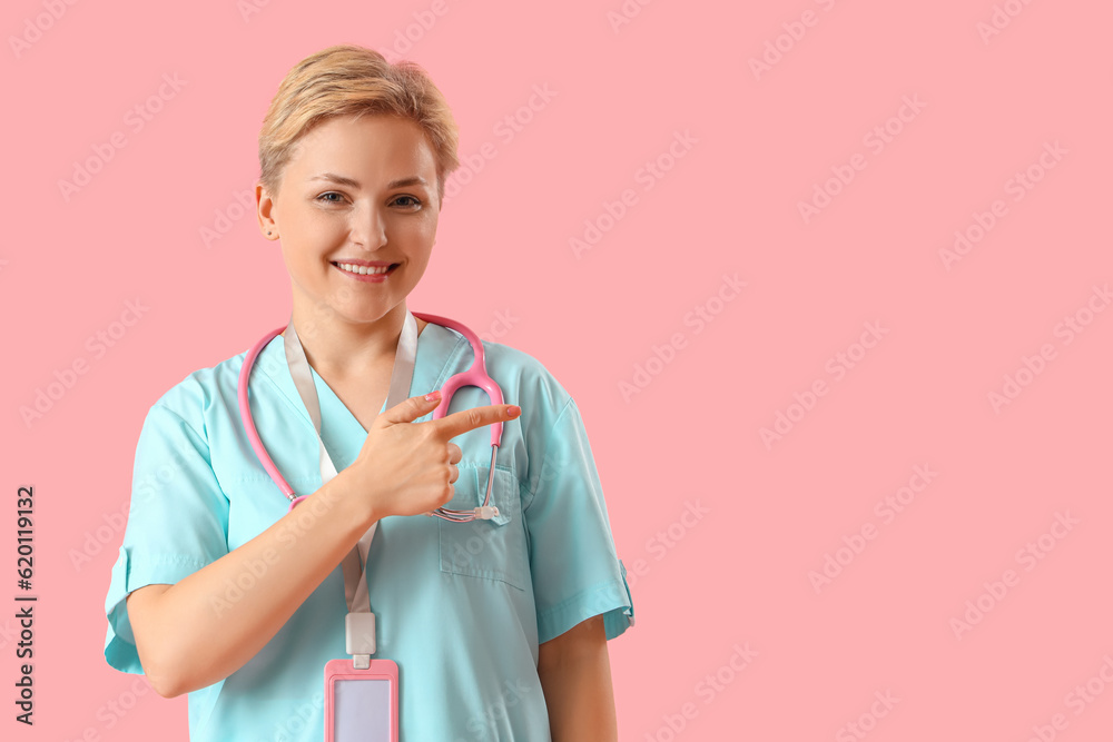Female medical intern pointing at something on pink background Female medical intern pointing at something on pink background