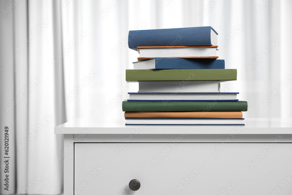 Fototapeta premium Hardcover books on white chest of drawers indoors