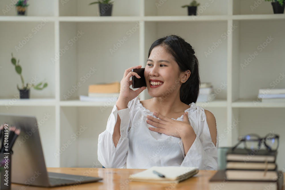 A young Asian businesswoman talking on her mobile phone while sitting at her working place in the office. A young Asian businesswoman talking on her mobile phone while sitting at her working place in the office.