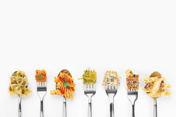 Forks and spoons with various tasty pasta on white background, flat lay. Space for text