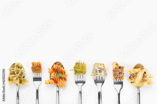 Fototapeta Forks and spoons with various tasty pasta on white background, flat lay