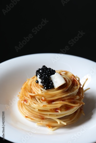 Tasty spaghetti with tomato sauce and black caviar on dark background, closeup. Exquisite presentation of pasta dish