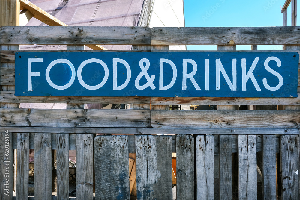 Obraz premium Großes bemaltes Holzschild mit der Aufschrift „Food & Drinks“ (deutsch: Essen & Trinken) draußen an einer Holzwand an einer angesagten Gastronomie