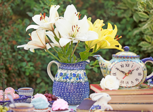 Beautiful ceramic jug with lilies on the table in the garden. Selective focus. photo