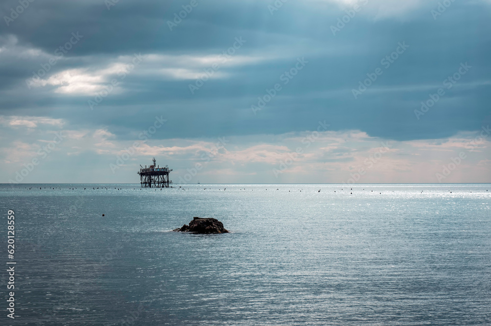 Fototapeta premium An abandoned offshore platform in the rays of the sun shining through thick clouds