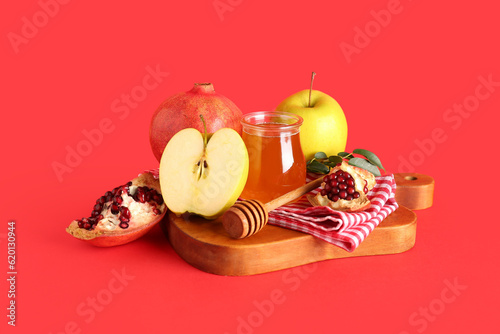 Bottle with jar of honey, pomegranate and apples for Rosh Hashanah celebration (Jewish New Year) on red background photo