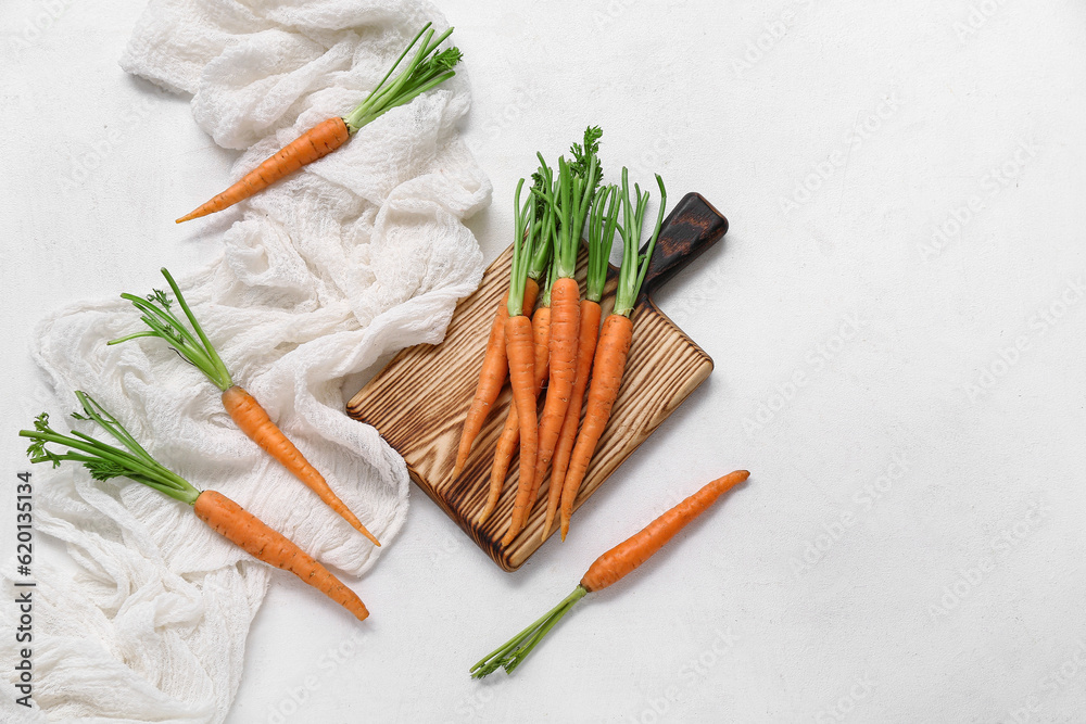 Wooden board of fresh carrots on white textured background