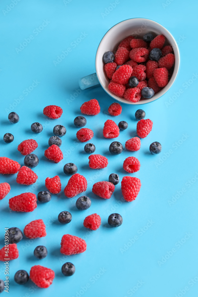 Cup with fresh raspberries and blueberries on blue background Cup with fresh raspberries and blueberries on blue background