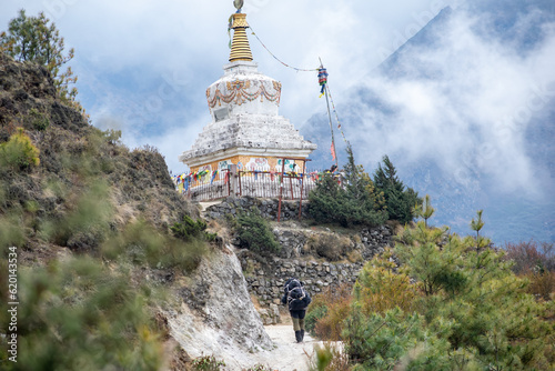 A trekker is hiking through sagarmatha national park in nepal. White colored stupa with clouds and mountains can be seen in the backdrop of hiker. Captured during trek to everest base camp in nepal. photo