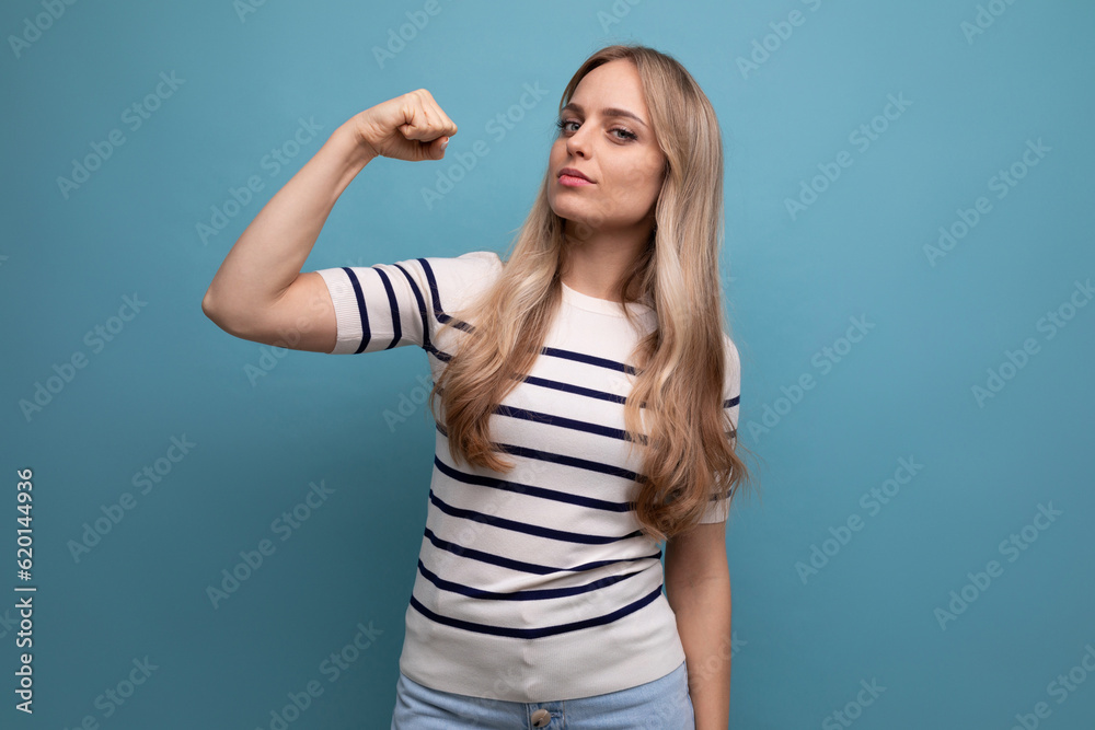 Fototapeta premium close-up photo of a strong girl in casual clothes showing biceps on a blue isolated background