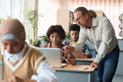 Canvas Print Mature teacher teaching group of foreign students during lesson in class