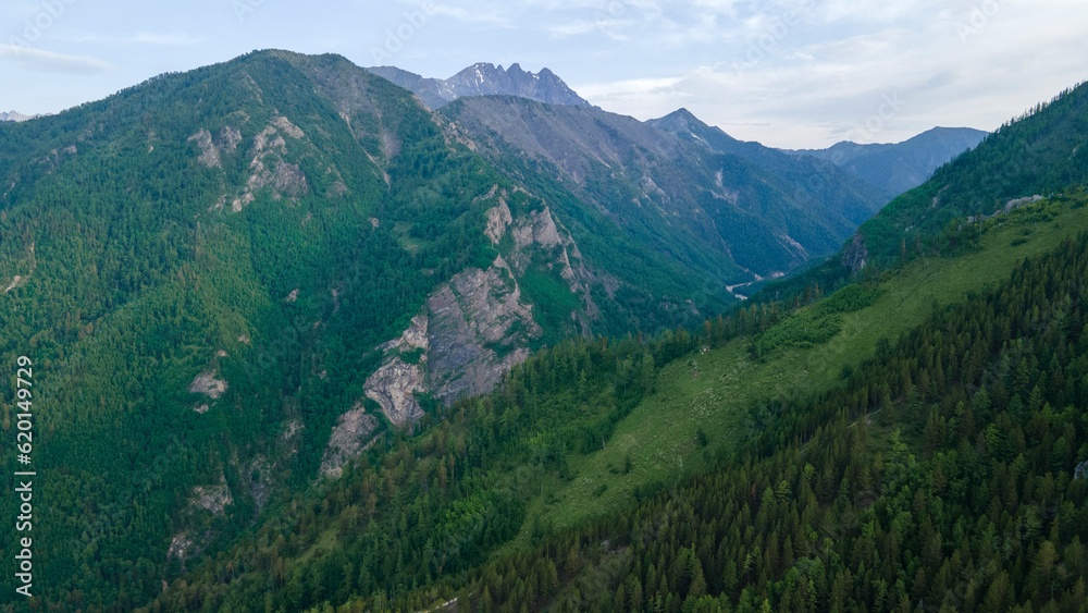 Aerial view of a high valley of the rocky mountain ridges, on which snow lies in places, near to the fast mountain river at summer cloud morning, blue picture Aerial view of a high valley of the rocky mountain ridges, on which snow lies in places, near to the fast mountain river at summer cloud morning, blue picture