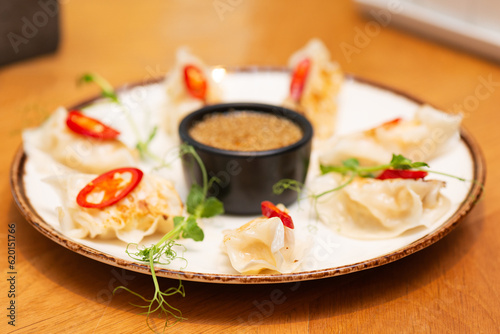 Gyoza or Japanese fried dumplings with chili, microgreens and sauce in a plate in a restaurant.