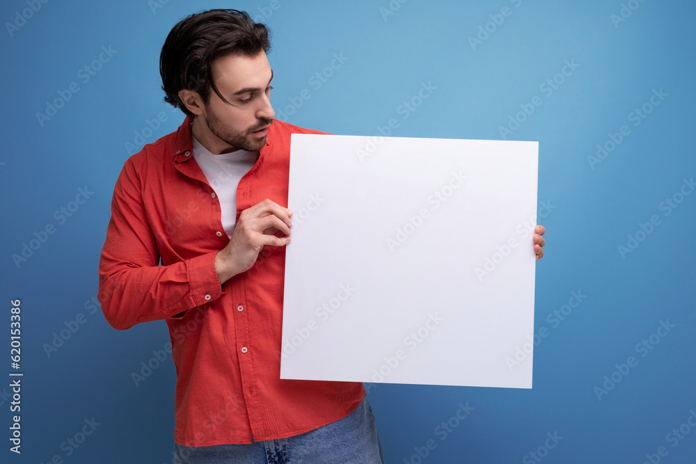 charming positive 30s man in red shirt holding white paper poster with mockup charming positive 30s man in red shirt holding white paper poster with mockup