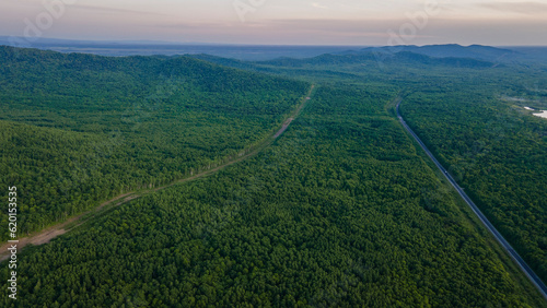 Aerial view of the country road and power lines near to the mountain range, coniferous high forest and the river at summer cloud sunset with horizon, orange color