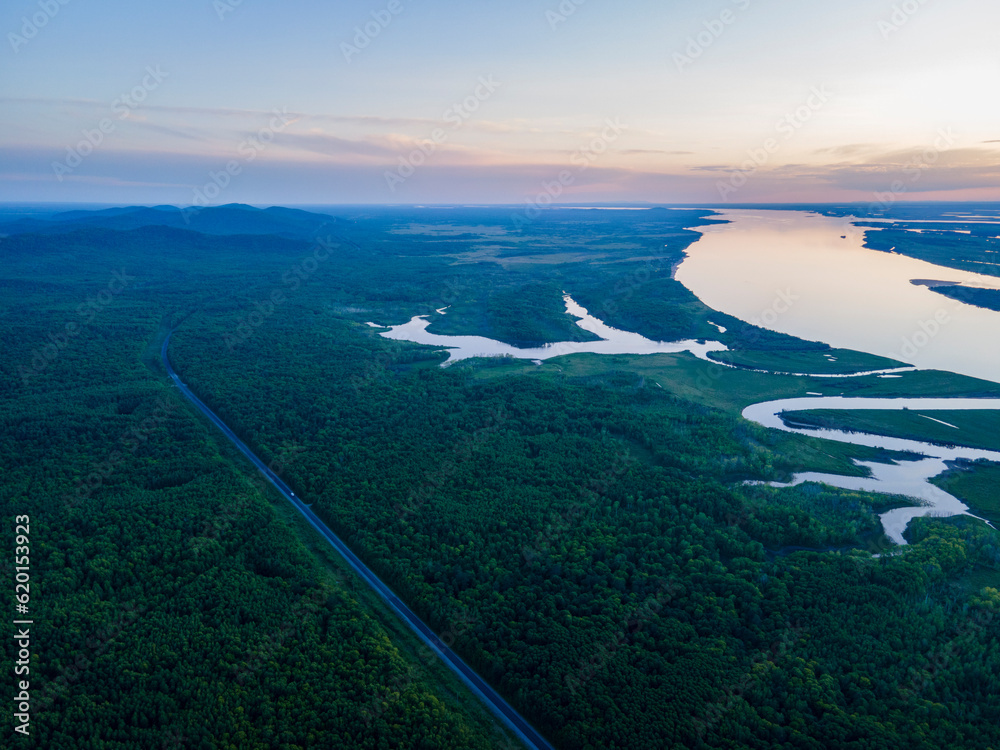 Aerial view of the clear big river near to the peak of the mountain range and tall forest at incredible  dark summer cloud evening with horizon