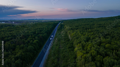 Aerial view of the slope of a mountain range and tall taiga near to the river at summer cloud evening with horizon