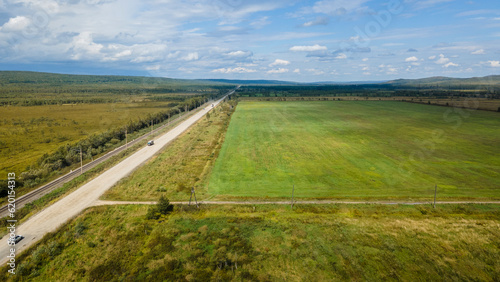 Aerial view of the country road and power lines near to the hill range, small coniferous forest and meadows agriculture at summer cloud sunny with horizon, orange, low height