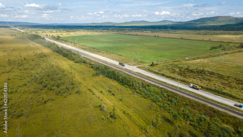 Aerial view of the country road and power lines near to the hill range, small coniferous forest and meadows agriculture at summer cloud sunny with horizon, shadows, color image, low height