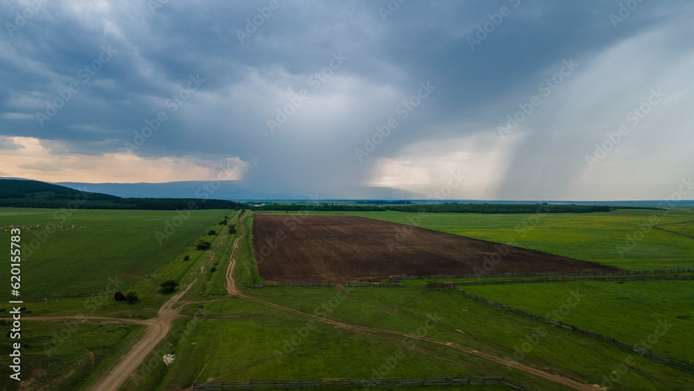 Naklejka premium Aerial view of the meadows with cows and horses near to the mountain ridge and country road at summer cloud rain day, blue color of the picture