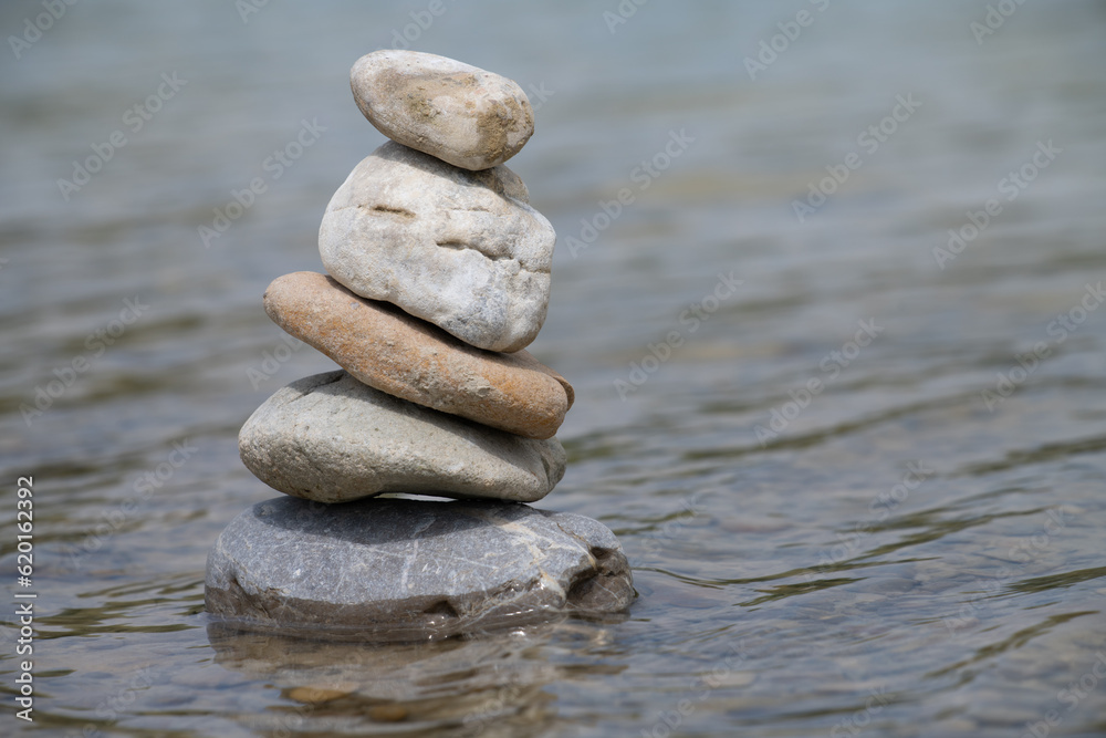 Several round pebbles of different sizes are stacked on top of each other. They form a pyramid. The stones stand in shallow water. There is space for text Several round pebbles of different sizes are stacked on top of each other. They form a pyramid. The stones stand in shallow water. There is space for text
