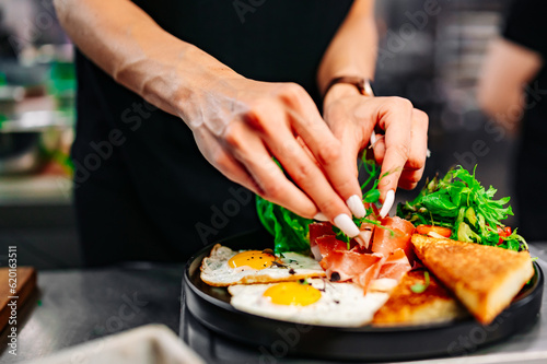 woman chef hand cooking fried eggs with ham, salad and hummus