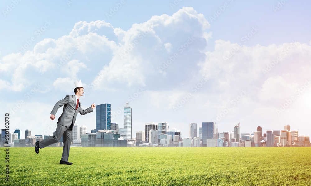 King businessman in elegant suit running on green grass and modern cityscape at background