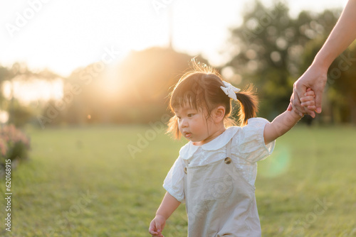 Asian mother walking with daughter in park, Parents hold the baby's hands, Happy family in the park evening light. Happy family concept