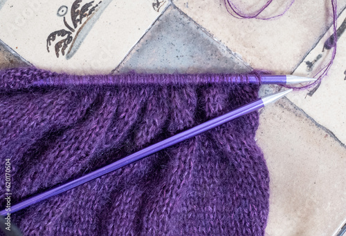 Close up of purple mohair and alpaca yarn hand knitted sweater with stitches including stocking stitch and rib, knitted on straight knitting needles. 