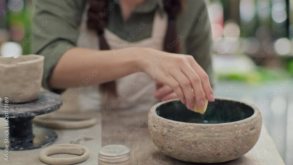 Medium close up of woman working with clay pot and making it wet with sponge in workshop Medium close up of woman working with clay pot and making it wet with sponge in workshop