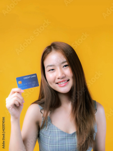 Asian girl showing credit card for payment shopping online and - paying by credit card isolated on yellow - online shopping e-commerce telemarketing concept