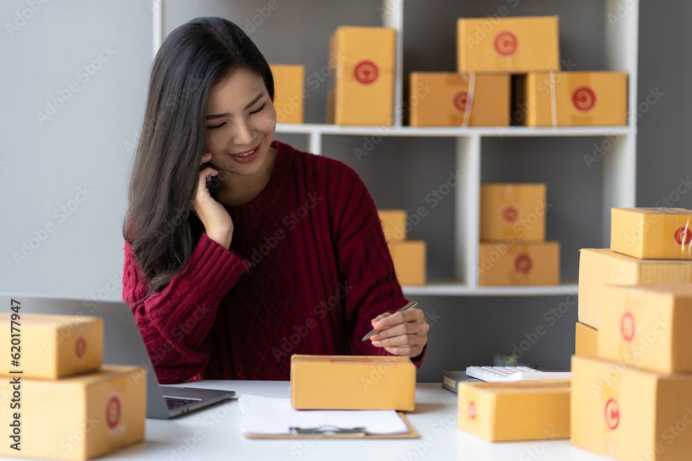 Female business owner holding parcel box for delivery and using smartphone to sell online at home office. SME business operators Female business owner holding parcel box for delivery and using smartphone to sell online at home office. SME business operators