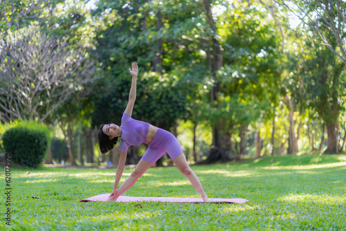 Asian woman doing yoga posing on mat in outdoor park Young healthy woman yoga exercise, yoga pose in natural environment for body, mind, health. Relax concept.