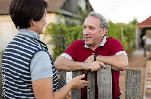 Two gardeners friendly talking outdoors next to wooden fence of country estate on day photo