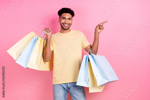 Portrait of pleasant cheerful man afro hair earrings stubble directing empty space hold shopping bags isolated on pink color background