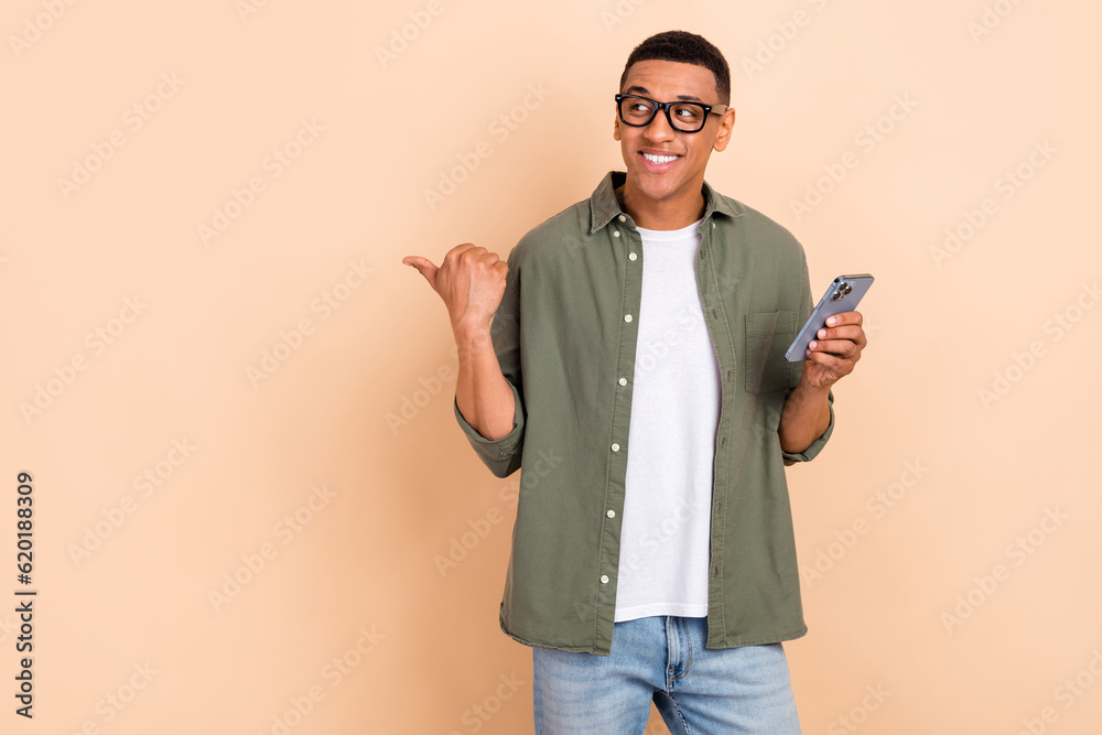 Portrait of optimistic man wear glasses stylish shirt look directing empty space hold smartphone isolated on beige color background