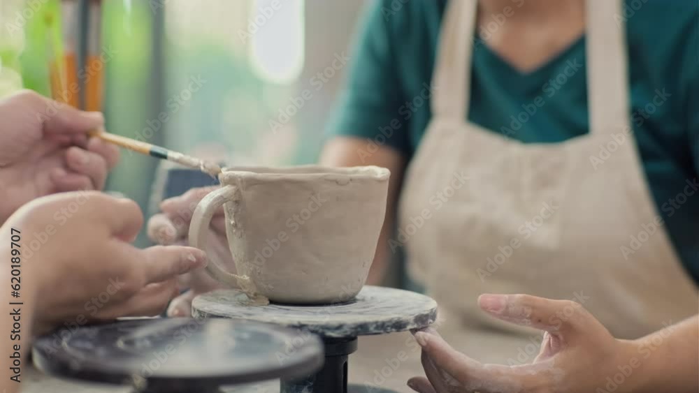 Medium close up of hands sculpting cup out of clay with brush