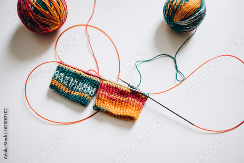 knitting with knitting needles by the magic loop method from multi-colored yarn on a white background