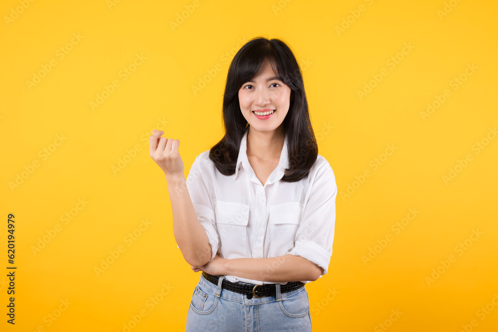 Thoughtful Asian woman keeps hand on chin looks pensively above wearing white shirt and jean plants poses against yellow background blank copy space for your advertising content thinks about future. Thoughtful Asian woman keeps hand on chin looks pensively above wearing white shirt and jean plants poses against yellow background blank copy space for your advertising content thinks about future.
