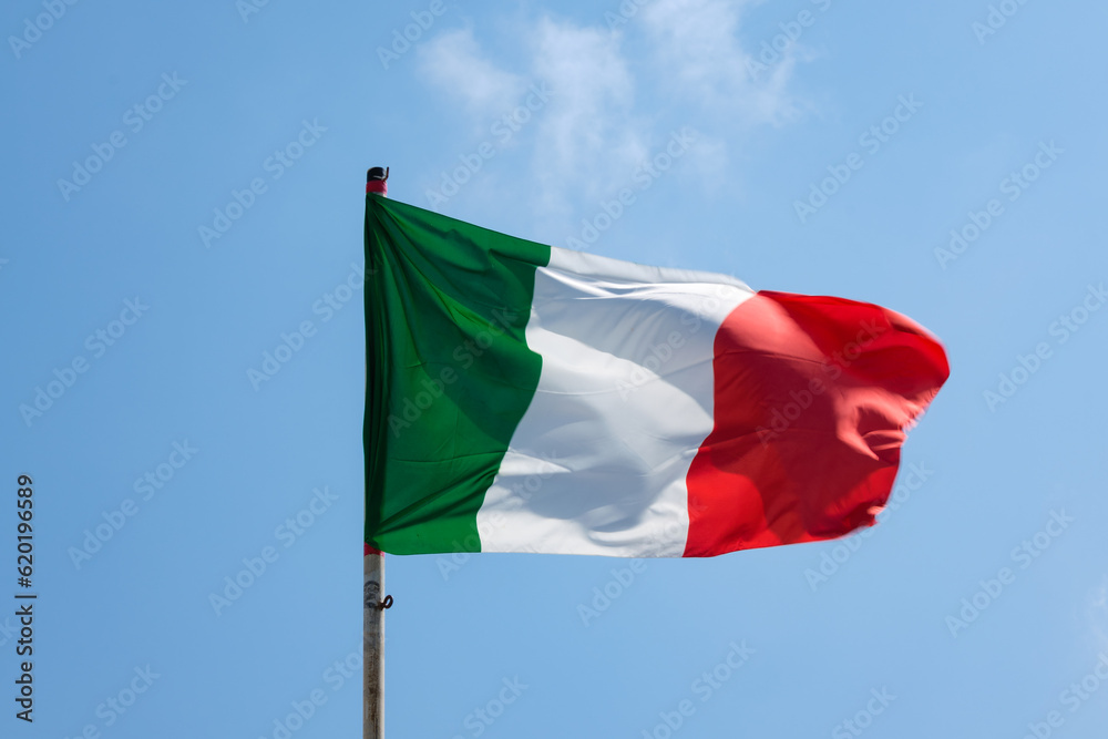 Italian tricolor flag waving with a clear sky in the background. Italian tricolor flag waving with a clear sky in the background.