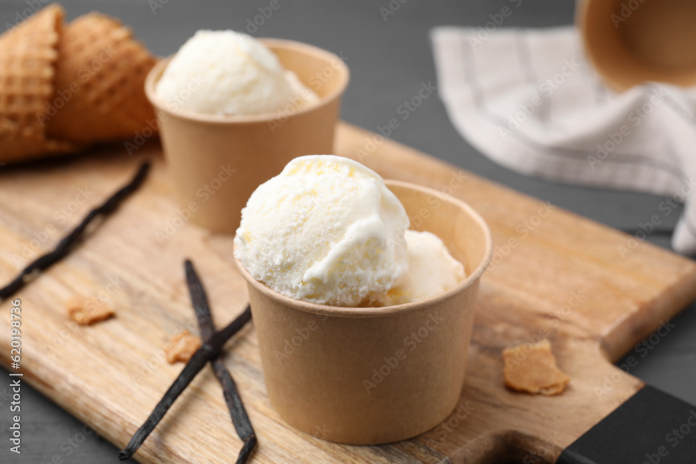 Paper cups with delicious ice cream and vanilla pods on wooden board, closeup Paper cups with delicious ice cream and vanilla pods on wooden board, closeup
