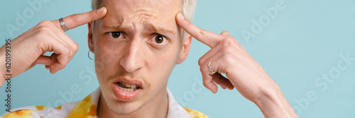 Young blonde man pointing fingers at his head while frowning