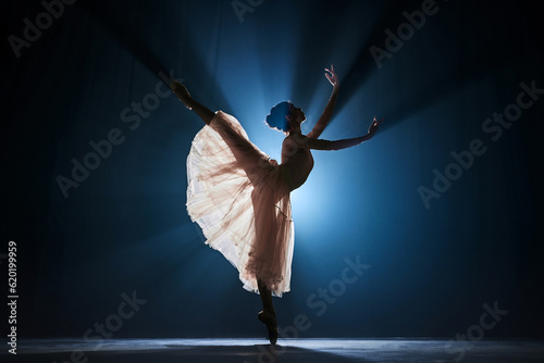Elegant, tender, slim, talented girl, female ballet dancing dancing against dark blue background with spotlight