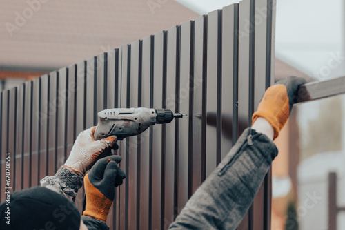 Leinwand Poster Workers install a metal profile fence