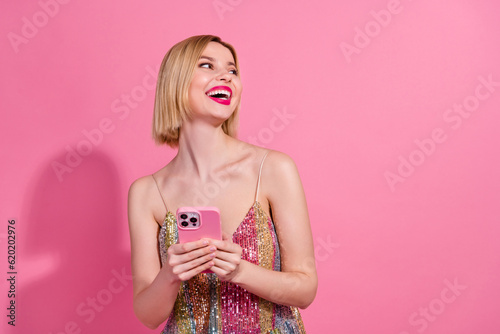 Photo of funny gorgeous pretty woman wear colorful dress hold smartphone look empty space laughing isolated on pink color background