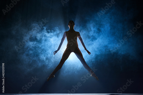 Elegant femininity. Beautiful, tender young woman, ballerina dancing against dark blue background with spotlight