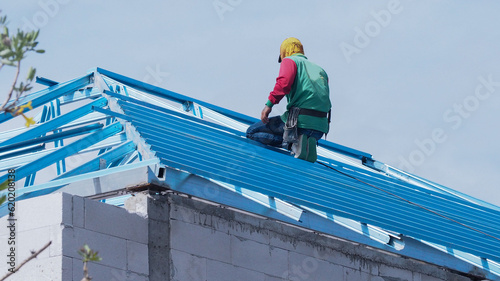 Workers are installing gray roof tiles wearing seat belts to ensure safe working at heights.