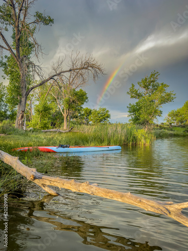 long and narrow racing stand up paddleboard at lake shore, stormy sky with rainbow