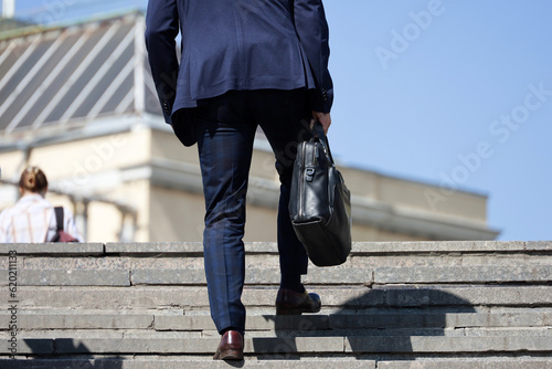 Man in a business suit with leather briefcase climbing stone stairs in city, male legs in motion on the steps. Concept of career, success, moving to the top, official or businessman